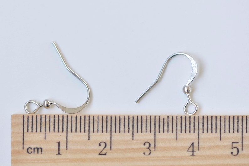 May include: Two silver earring hooks with a small ball at the top of the hook. The hooks are measured against a ruler, showing they are approximately 2 cm long.