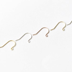 May include: Five earring hooks in different metal finishes: silver, gold, rose gold, and two shades of gold. The hooks are arranged in a diagonal line on a white background.
