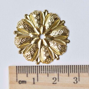 May include: Gold metal decorative embellishment with a floral design. The embellishment measures approximately 2 cm in diameter.