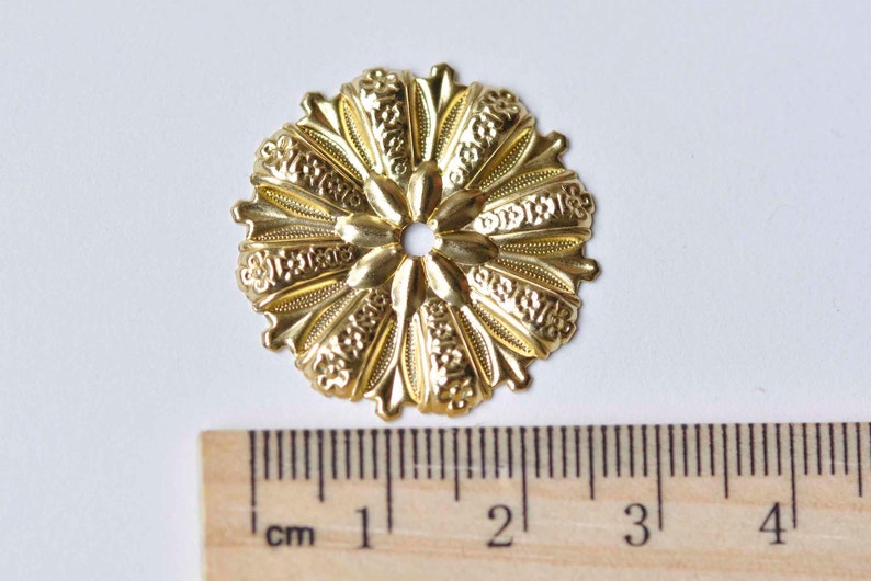May include: Gold metal decorative embellishment with a floral design. The embellishment measures approximately 2 cm in diameter.