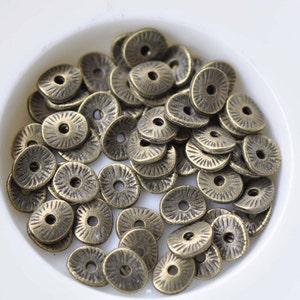 Peut inclure: Un tas de perles en métal de couleur or antique avec un motif en relief. Les perles sont de forme ovale avec un trou au centre.