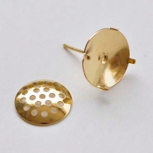 Puede incluir: Dos engastes para pendientes de color dorado. Un engaste tiene una base redonda y plana con un pequeño agujero en el centro. El otro engaste tiene una base redonda y plana con un patrón de pequeños agujeros.