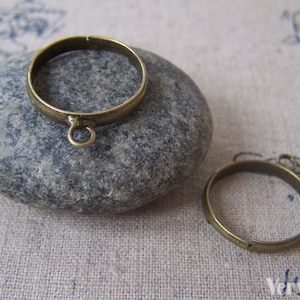 May include: Two antique brass metal rings with a jump ring attached to one of the rings. The rings are on a gray stone surface.