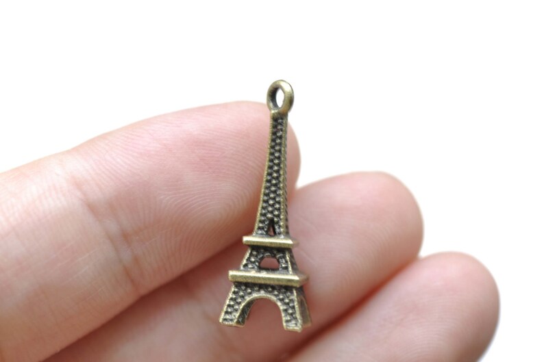 May include: A bronze-colored Eiffel Tower charm with a loop at the top for attaching to a necklace or bracelet.