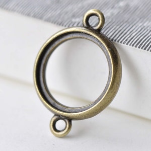 May include: A round, antique gold-toned metal pendant with two jump rings. The pendant has a circular opening in the centre.