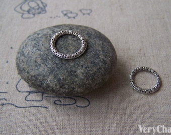 May include: Two silver metal rings with a textured design. The rings are on a gray stone and a gray fabric background.