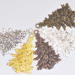 Pode incluir: Quatro pingentes de árvore de Natal de metal em diferentes acabamentos: prata, ouro, bronze e latão antigo. Cada pingente tem um design detalhado e um laço para pendurar.