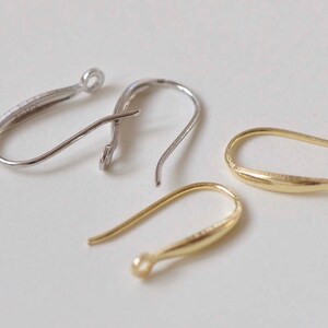May include: Three earring hooks in different finishes: silver, gold, and a lighter gold. The hooks are all made of metal and have a simple, elegant design.