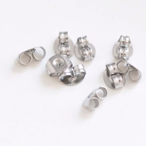May include: A close-up of a group of silver earring backs. The backs are made of metal and have a small loop on the back to secure the earring.