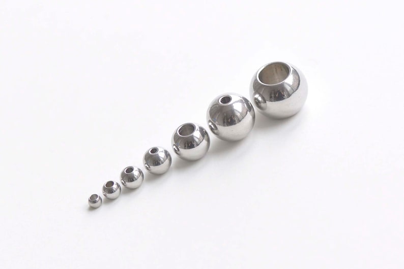 May include: A set of eight silver metal beads of varying sizes. The beads are round and have a hole in the center.