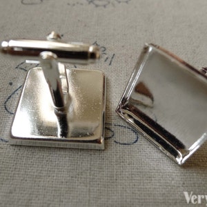 Puede incluir: Un par de gemelos de plata con inserciones de vidrio de forma cuadrada. Los gemelos están diseñados para ser personalizados con imágenes o texto.