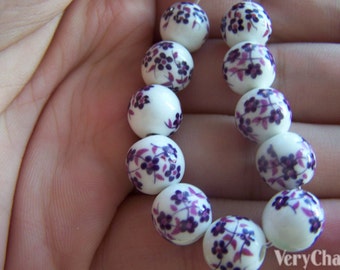Può includere: Una collana di perle bianche con motivi floreali viola. Le perle sono infilate su un cordoncino elastico trasparente.