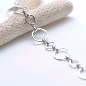 May include: A silver chain necklace with large, linked, circular pendant charms.