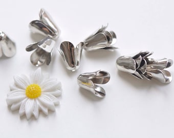 以下が含まれることがあります： 銀色の金属製のフラワーシェイプの装飾品のコレクション。花びらが複数層になっているものもあります。白いデイジーが1つ、黄色い中心があります。