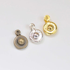 May include: Three metal button closures in gold, silver, and bronze. Each button has a round, raised center and a flat, circular base.