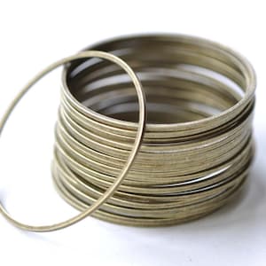 Può includere: Un mucchio di anelli di metallo color oro, ogni anello è un semplice cerchio con una finitura liscia.