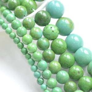 May include: A strand of round, green turquoise beads of varying sizes. The beads are strung on a clear thread and are arranged in a graduated pattern, with the largest beads at the bottom and the smallest beads at the top.