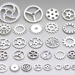 May include: A collection of 27 silver metal gears of various sizes and designs. The gears are arranged in a random pattern on a grey background.