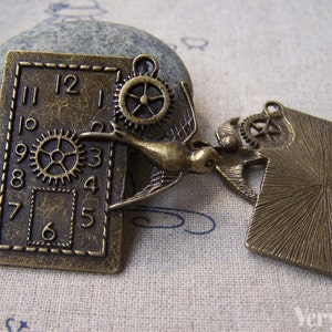 Peut inclure: Deux breloques en bronze antique, l'une avec un cadran d'horloge et des engrenages, l'autre avec un oiseau et des engrenages. Les deux breloques ont une surface texturée et un aspect vieilli.