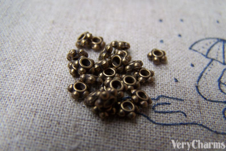 May include: A close-up of a pile of small, gold-colored metal beads. The beads are round with a small hole in the center and have a decorative design around the edge.