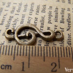 May include: A bronze-colored metal charm shaped like a treble clef. The charm is about 1 inch long and is measured against a ruler.