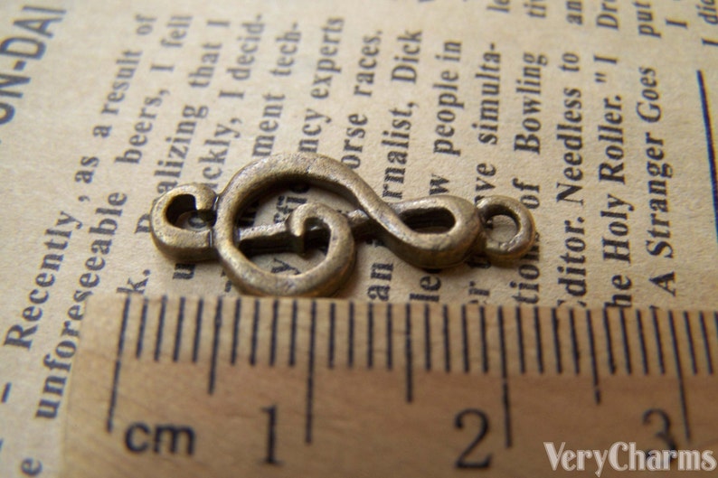 May include: A bronze-colored metal charm shaped like a treble clef. The charm is about 1 inch long and is measured against a ruler.