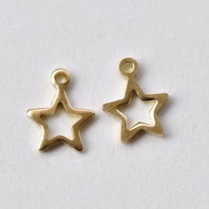 Könnte beinhalten: Zwei goldfarbene Metall-Stern-Anhänger mit einem Loch oben zum Anbringen an Schmuck oder anderen Bastelarbeiten.