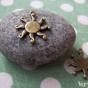 May include: Two gold-toned metal sun charms with a decorative design. The charms are on a green and white polka dot background.