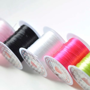 May include: Five spools of elastic cord in different colors: pink, black, white, hot pink, and lime green. The spools are all white with a diamond logo and text.