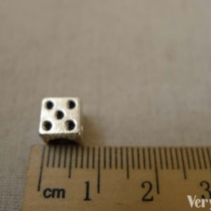 May include: A silver metal dice charm with five black dots, measuring 1 cm in size.