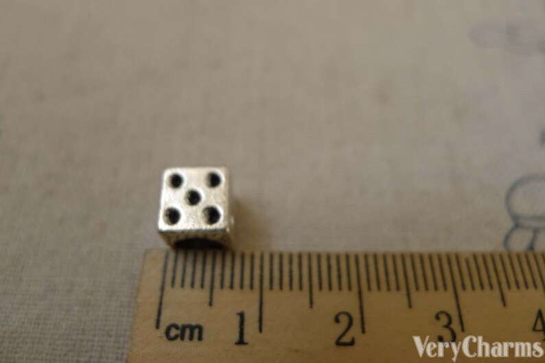 May include: A silver metal dice charm with five black dots, measuring 1 cm in size.
