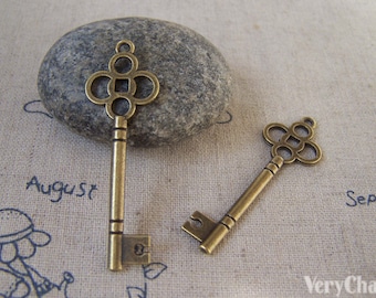 May include: Two antique gold-toned skeleton keys with ornate keyholes. The larger key is on a gray stone. The smaller key is on a beige fabric background.