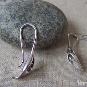 Puede incluir: Dos ganchos para pendientes de plata con un diseño curvo en forma de hoja. Los ganchos son de metal y tienen un acabado brillante.