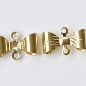 Könnte beinhalten: Zwei goldfarbene Metallschließen in Bogenform, jede mit drei Ösen. Die Schließen sind als Verschluss für Halsketten oder Armbänder gedacht.
