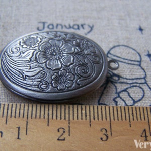 May include: A silver oval locket with an engraved floral design. The locket is approximately 2 cm in length.