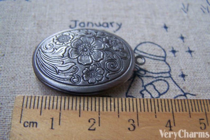 May include: A silver oval locket with an engraved floral design. The locket is approximately 2 cm in length.