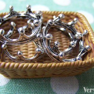 Puede incluir: Cuatro separadores de anillos en forma de corona plateados en una cesta de mimbre tejida. Los separadores est&aacute;n intrincadamente detallados y tienen un acabado brillante.
