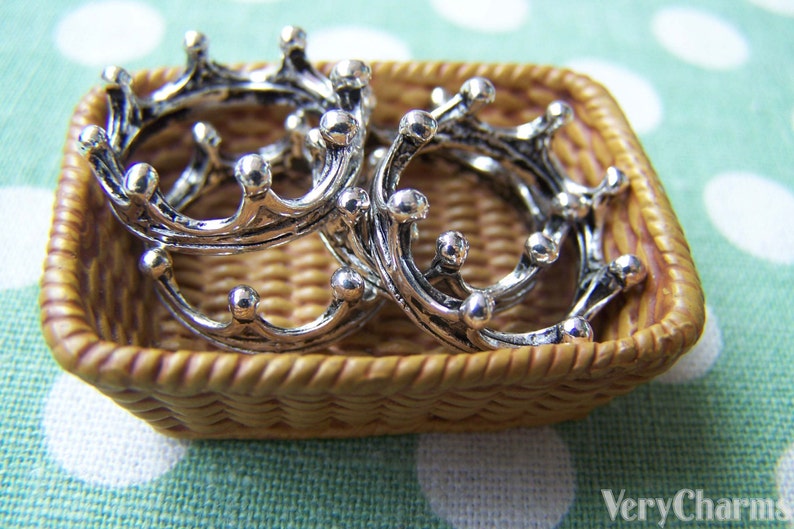 Puede incluir: Cuatro separadores de anillos en forma de corona plateados en una cesta de mimbre tejida. Los separadores est&aacute;n intrincadamente detallados y tienen un acabado brillante.