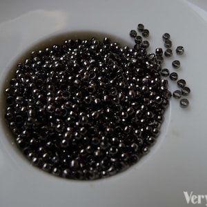 May include: A close-up of a white plate filled with black metal beads. The beads are small and round, and they are arranged in a pile in the center of the plate.