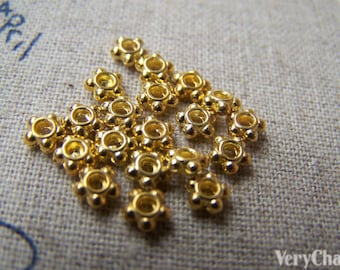 May include: A group of 18 gold-colored metal beads with a starburst design. The beads are arranged in a cluster on a beige fabric surface.