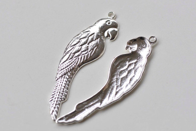 May include: Two silver parrot charms with detailed wing and feather designs. The charms have a loop at the top for attaching to jewelry or other crafts.