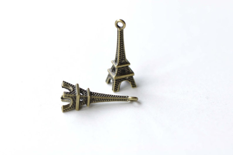 May include: Two small, gold-colored Eiffel Tower charms. The charms are detailed and have a textured surface.