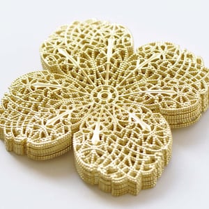 Könnte beinhalten: Ein goldfarbener, metallischer Blumenschmuck mit einem filigranen, komplizierten Design. Die Blume besteht aus mehreren Metallschichten, die einen dreidimensionalen Effekt erzeugen.