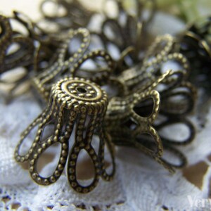 May include: A group of antique gold-toned metal decorative embellishments with a scalloped design. The embellishments are arranged on a white lace surface.