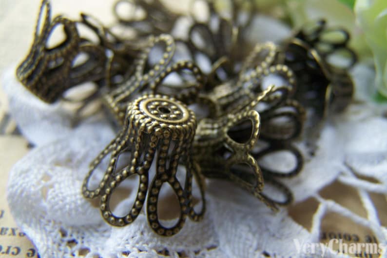 May include: A group of antique gold-toned metal decorative embellishments with a scalloped design. The embellishments are arranged on a white lace surface.