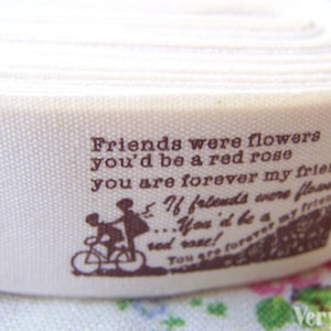 May include: White cotton ribbon with brown text that reads "Friends were flowers you'd be a red rose you are forever my friend". The ribbon features a silhouette of two people riding a bicycle.