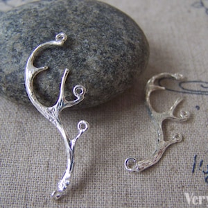 May include: Two silver-toned metal charms shaped like branches with textured details. Each charm has a loop at the top and a few smaller loops along the branches.