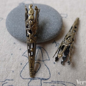 May include: Two ornate metal cone-shaped bead caps with a filigree design. The caps are a gold color and have a textured surface.