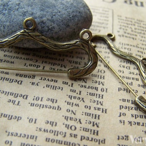 Peut inclure: Une épingle de sûreté de couleur bronze avec un design décoratif en forme de brindille. L'épingle est ouverte et l'épingle de sûreté est visible.