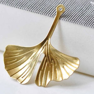Puede incluir: Un dije de hoja de ginkgo de metal dorado con un agujero en la parte superior para sujetarlo a joyas u otras manualidades.